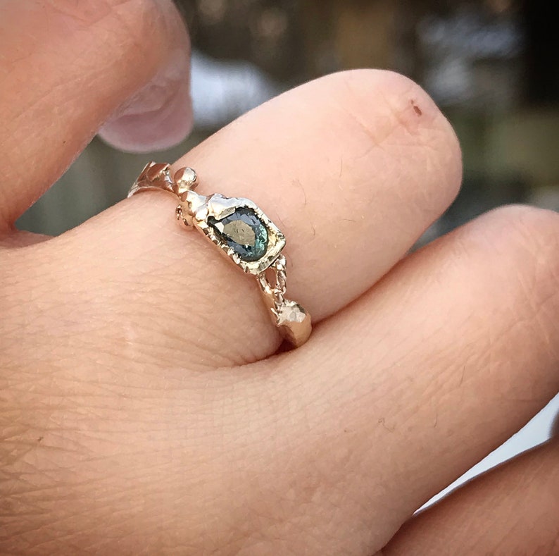 May include: A gold ring with a green gemstone set in a textured band. The ring is on a person's finger.