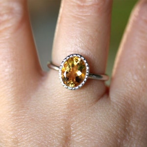 Puede incluir: Un anillo de plata con una gran piedra preciosa ovalada de topacio. La piedra preciosa es de color naranja claro y tiene un corte facetado.