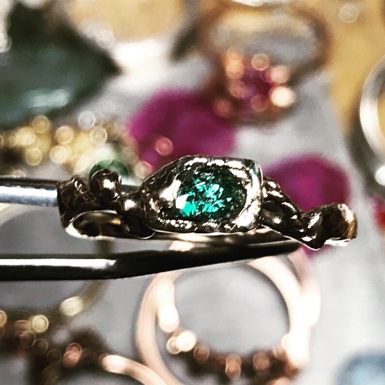 May include: A green gemstone ring with a twisted band setting. The ring is made of gold and has a rustic, organic look.