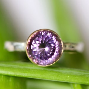 May include: A silver ring with a round, faceted, purple gemstone set in a bezel setting.