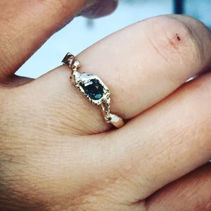 May include: A gold ring with a twisted band and a dark blue gemstone set in a square bezel.
