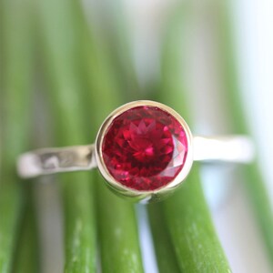 May include: A silver ring with a large, oval-shaped, bright red gemstone.