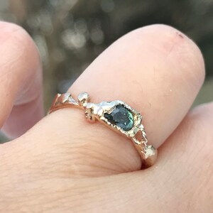 May include: A gold ring with a unique, organic design features a dark green gemstone set in a rough, textured setting.