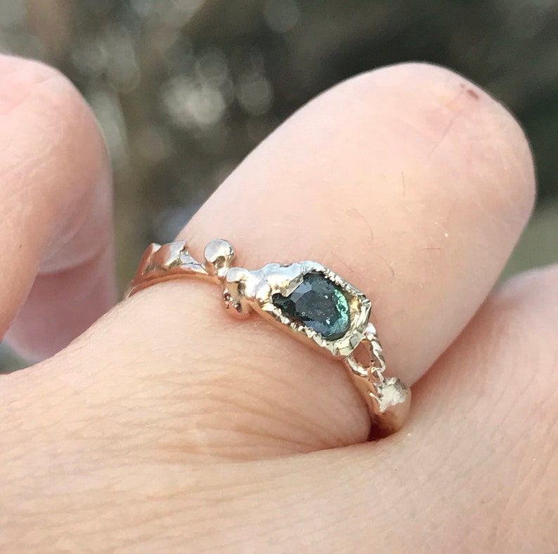 May include: A gold ring with a unique, organic design features a dark green gemstone set in a rough, textured setting.