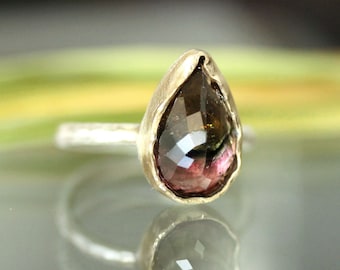 Könnte beinhalten: Ein silberner Ring mit einem tropfenförmigen Edelstein. Der Edelstein ist tiefrosa mit grünen und braunen Einschlüssen.