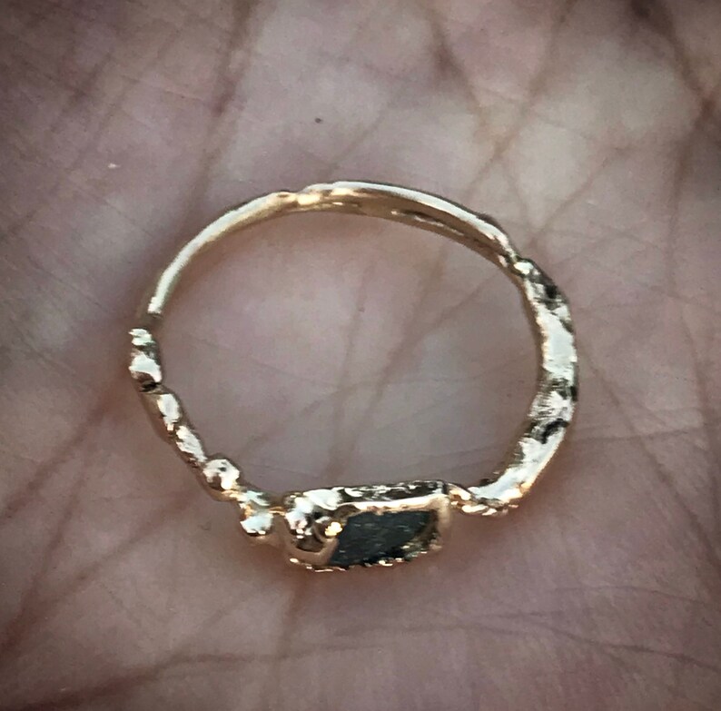 May include: A gold ring with a textured band and a black stone set in a gold bezel.