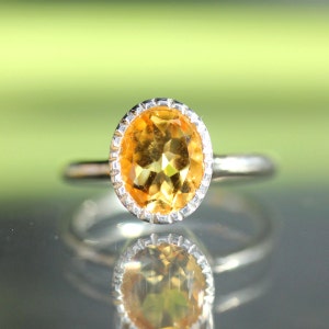 Puede incluir: Un anillo de plata con una piedra preciosa de citrino amarillo redonda y facetada engastada en un engaste de plata.