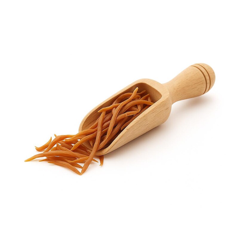 May include: A wooden scoop filled with orange-brown pasta. The scoop has a handle and is made of light-colored wood. The pasta spills out of the scoop onto a white surface. The pasta is long and thin, with a slightly curved shape.