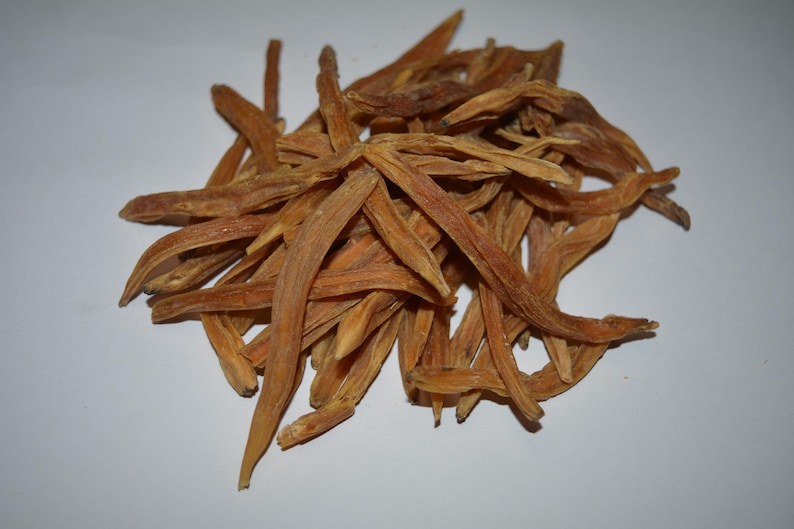May include: A pile of dried, light brown, elongated roots. The roots have a slightly curved shape and a rough texture. They are arranged in a loose heap against a white background. The color is consistent throughout the pile.