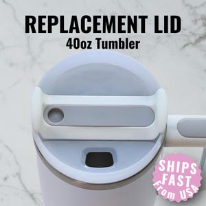 May include: Replacement lid for a 40oz tumbler. The lid is light gray and white, with a handle and a sliding closure. The text "REPLACEMENT LID" and "40oz Tumbler" are printed in black.