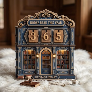 May include: A navy blue and gold wooden bookshelf-shaped display with the text "BOOKS READ THIS YEAR" and the numbers "365". The display has a library theme with miniature books, a coffee cup, and the text "OLIVIA'S LIBRARY".