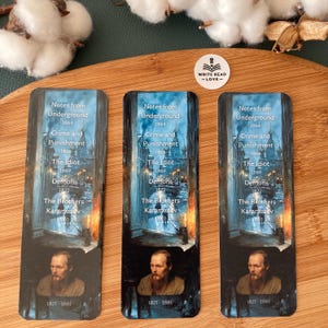 May include: Three rectangular bookmarks featuring a portrait of a man and titles of literary works. The titles include "Notes from Underground," "Crime and Punishment," and "The Brothers Karamazov." The bookmarks have a dark, artistic design.