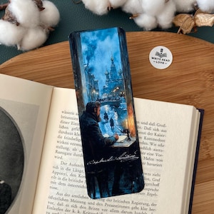 May include: A bookmark featuring a detailed illustration of a man writing at a desk, with a cityscape visible through a window. The scene is rendered in cool tones, with a focus on the man and the architecture. The bookmark has the text "WRITE READ -LOVE-".