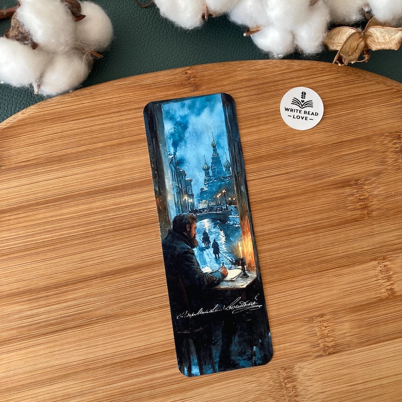 May include: A rectangular bookmark featuring a painting of a man writing at a desk, with a snowy cityscape visible through a window. The scene is predominantly blue and white, with a warm glow from a lamp. The text "WRITE READ -LOVE-" is also visible.