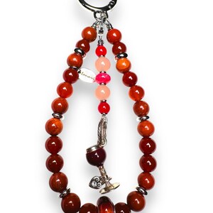 May include: A red, orange and pink beaded keychain with a silver charm of a wine glass. The keychain has a silver ring at the top.