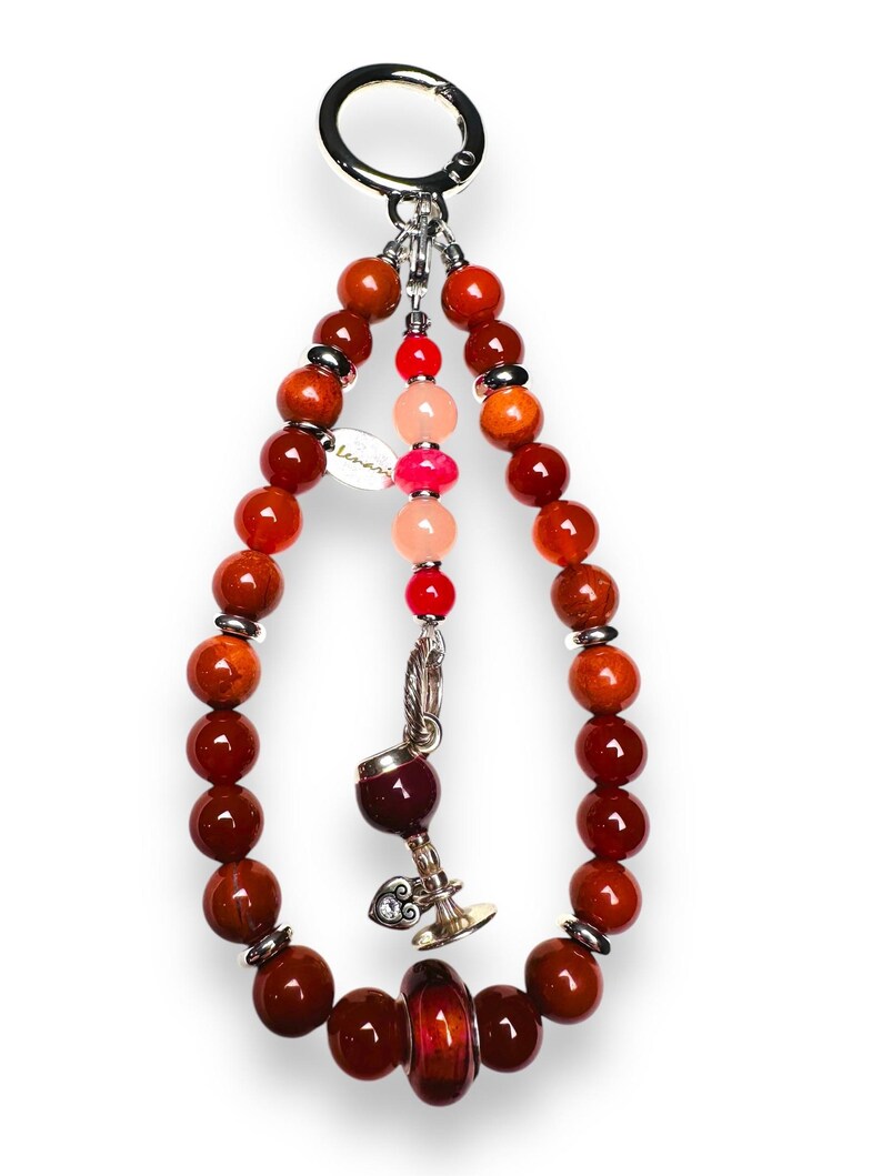 May include: A red, orange and pink beaded keychain with a silver charm of a wine glass. The keychain has a silver ring at the top.