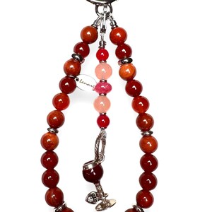 May include: A red, orange and pink beaded keychain with a silver charm of a wine glass. The keychain has a silver ring at the top and a small tag that says "Lemari".