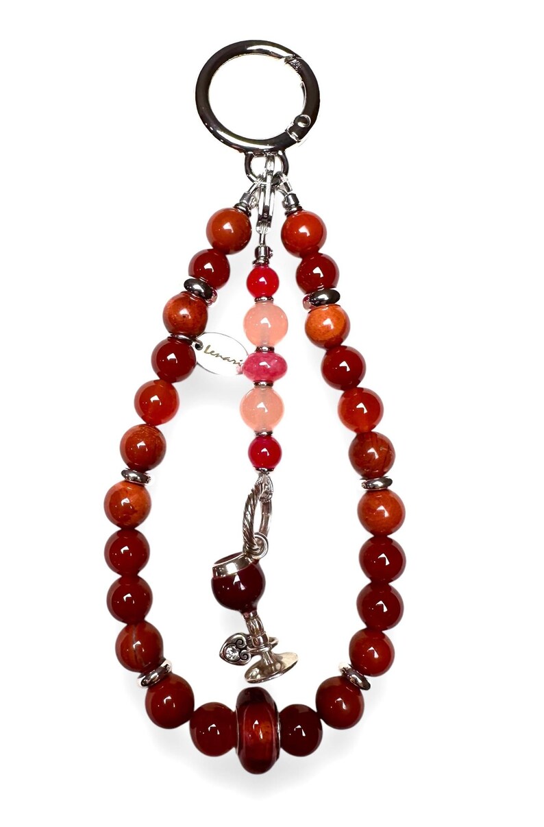 May include: A red, orange and pink beaded keychain with a silver charm of a wine glass. The keychain has a silver ring at the top and a small tag that says "Lemari".