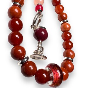 May include: A red and orange beaded bracelet with a silver charm and a glass bead with a red and orange swirl pattern. The charm has a heart with the word "Love" on it.