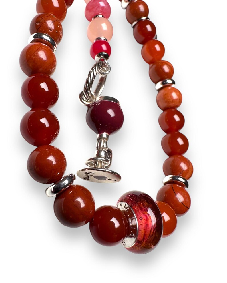May include: A red and orange beaded bracelet with a silver charm and a glass bead with a red and orange swirl pattern. The charm has a heart with the word "Love" on it.
