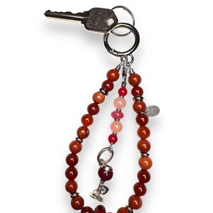 May include: A red, orange and pink beaded keyring with a silver charm of a wine glass. The keyring is attached to a silver key ring.