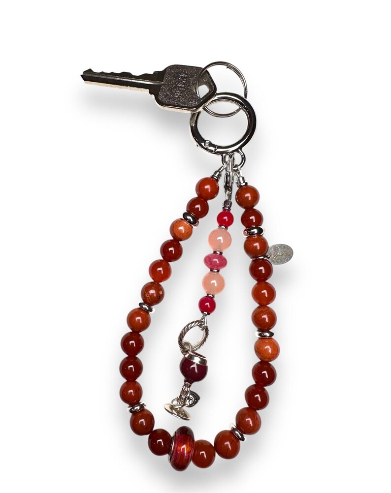 May include: A red, orange and pink beaded keyring with a silver charm of a wine glass. The keyring is attached to a silver key ring.