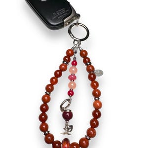 May include: A red, orange and pink beaded keychain with a silver wine glass charm and a silver key ring. The keychain is attached to a black car key fob with the text "POS ID: HW1144CE 1711001-1441 007611-001441-5100 DENSO 144CK"