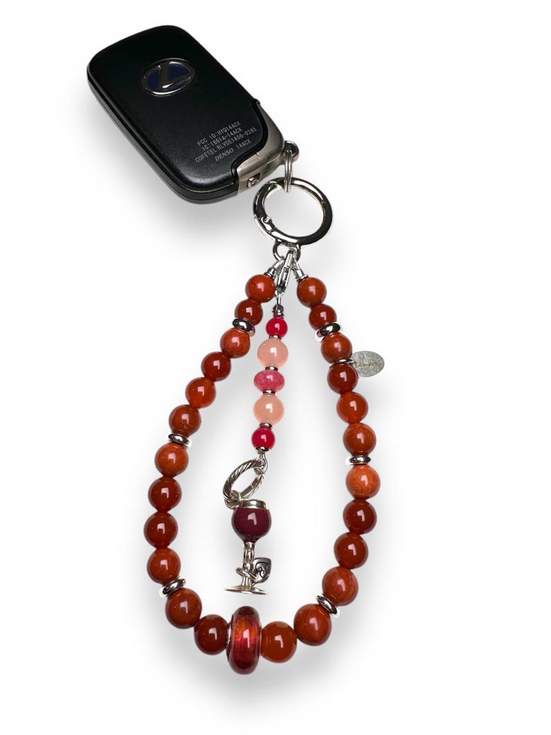 May include: A red, orange and pink beaded keychain with a silver wine glass charm and a silver key ring. The keychain is attached to a black car key fob with the text "POS ID: HW1144CE 1711001-1441 007611-001441-5100 DENSO 144CK"