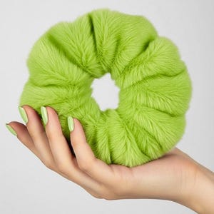 May include: A bright lime green hair scrunchie with a soft, fuzzy, faux fur texture. The circular accessory features a gathered, pleated design around a central opening, creating a voluminous and plush appearance for securing hair in place.