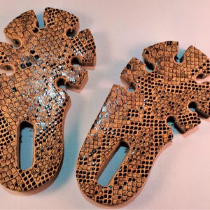 Può includere: Due tappi decorativi in legno per bottiglie di vino. I tappi hanno una forma unica con un ritaglio e un motivo a pelle di serpente strutturato in tonalità marroni e nere. Accenti glitterati argentati aggiungono un tocco di brillantezza.