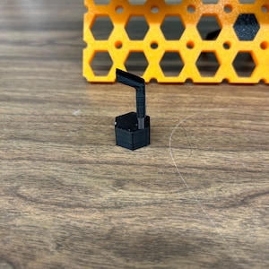 May include: A black plastic 3D printed model of a small chimney with a curved pipe.