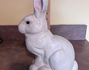 May include: A white ceramic rabbit figurine with a crackled glaze. The rabbit is sitting with its ears upright and has a black eye.