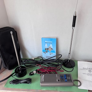 May include: A collection of CB radio equipment, including a black carrying case, two antennas, a handheld radio, and various cables. A blue and white "Owner's Manual" and a document titled "Plain English Rules" are also present.