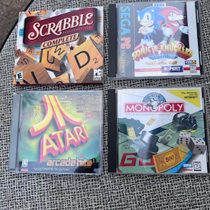 May include: Four PC game cases are displayed. Titles include "Scrabble Complete", "Sonic & Knuckles", "Atari Arcade Hits", and "Monopoly". The games are in their original packaging, with colorful graphics and text.