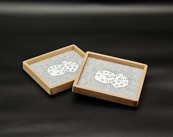 May include: Two square wooden dice trays with light gray felt interiors. Each tray features a white graphic of two dice. The trays are set against a dark gray background.