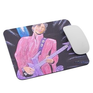 May include: Rectangular mousepad featuring a vibrant illustration of a musician in a pink suit playing a purple guitar. The background is dark with blue and white accents. A white computer mouse is placed on the right side of the mousepad.