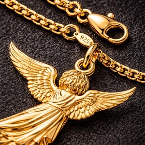 Puede incluir: Collar con colgante de &aacute;ngel dorado. El colgante presenta un &aacute;ngel con las alas extendidas. La cadena del collar es de estilo eslabones con un cierre de mosquet&oacute;n. El cierre y el colgante son de color dorado brillante. El collar est&aacute; sobre un fondo negro.