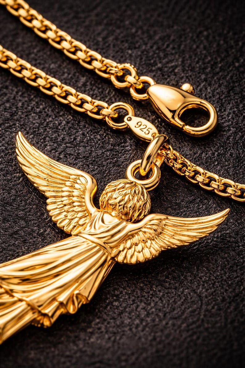 Puede incluir: Collar con colgante de &aacute;ngel dorado. El colgante presenta un &aacute;ngel con las alas extendidas. La cadena del collar es de estilo eslabones con un cierre de mosquet&oacute;n. El cierre y el colgante son de color dorado brillante. El collar est&aacute; sobre un fondo negro.