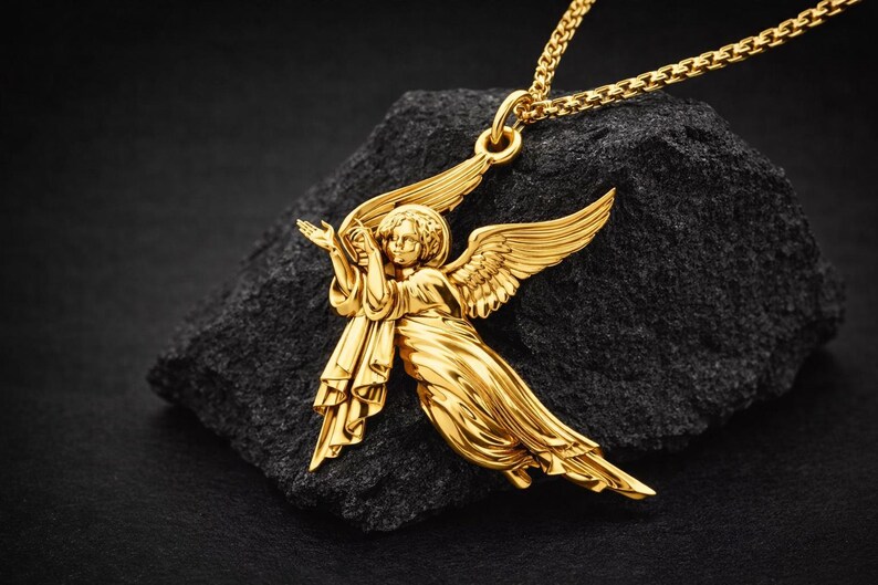 Puede incluir: Un collar con colgante de &aacute;ngel dorado. El colgante presenta un &aacute;ngel con alas extendidas y t&uacute;nicas fluidas. El collar se exhibe sobre una roca oscura y texturizada sobre un fondo negro.