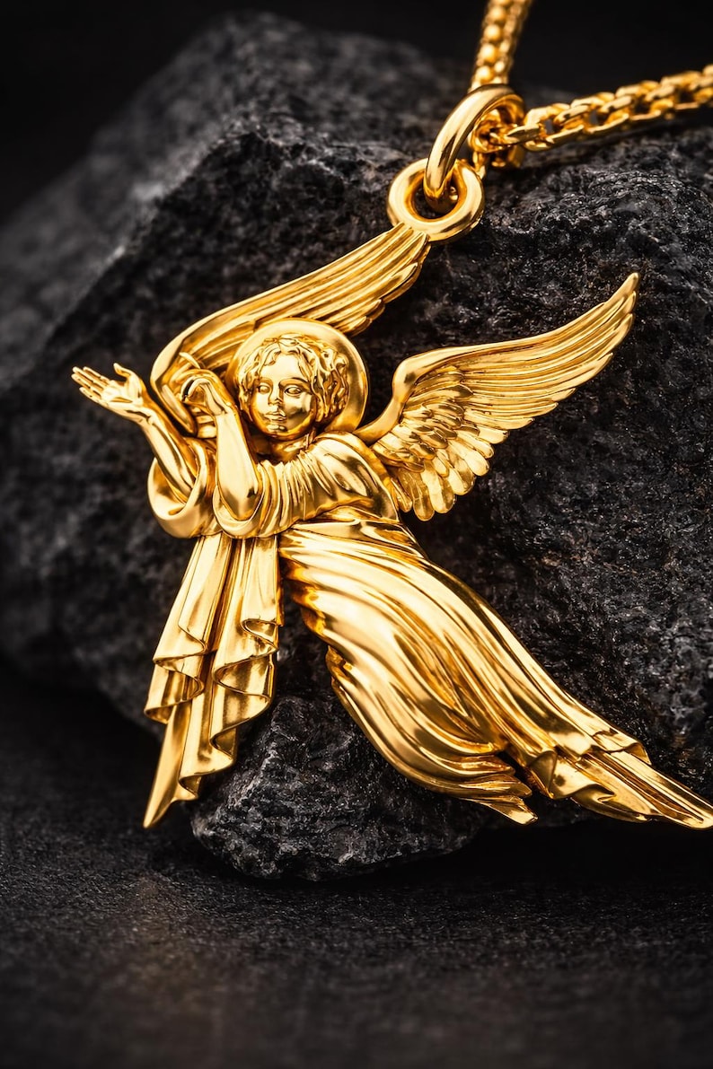 Puede incluir: Un collar con colgante de &aacute;ngel dorado. El colgante presenta un &aacute;ngel con alas extendidas y ropajes fluidos. El collar se muestra sobre una superficie oscura y texturizada, resaltando los intrincados detalles de la joya.