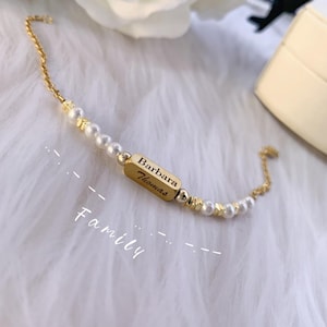 May include: A gold chain bracelet with white pearls and a gold bar charm engraved with the names "Barbara Thomas" and the word "Family".