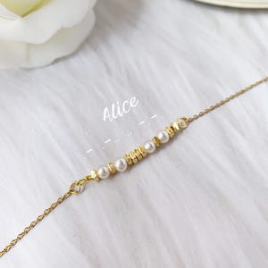 以下が含まれることがあります： 繊細なパールとゴールドビーズのデザインが施されたゴールドチェーンネックレス。ネックレスには「Alice」という名前が書かれています。