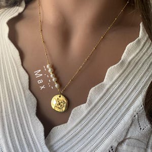 May include: Gold necklace with a round pendant featuring a dog's face and a strand of pearls. The necklace is labeled "Max".