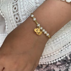 May include: A gold bracelet with white pearls and two gold heart charms with the initials "KA" engraved on them.