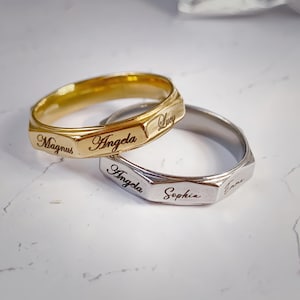 Può includere: Due anelli personalizzati, uno dorato e uno argentato, con nomi incisi. L'anello dorato ha i nomi "Magnus", "Angela" e "Lucy". L'anello argentato ha i nomi "Angela", "Sophia" e "Emma".