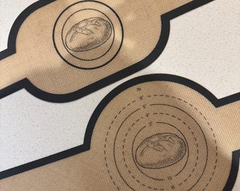 Könnte beinhalten: Zwei braune Silikon-Backmatten mit schwarzen Rändern. Eine Matte hat einen Kreis mit konzentrischen Kreisen und Maßen in Zoll und Zentimetern. Die andere Matte hat einen einzelnen Kreis mit einer Illustration eines Laibes Brot. Beide Matten haben eine Illustration eines Laibes Brot.