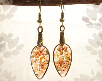 Può includere: Orecchini a goccia con fiori arancioni secchi racchiusi in resina trasparente. Gli orecchini hanno elementi metallici color ottone antico e ganci per le orecchie dorati. Sono appesi a un ramo marrone, lunghi circa 4 cm.