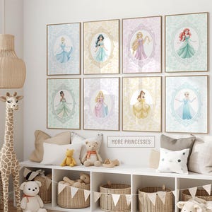 Peut inclure: Huit cadres muraux représentant diverses princesses animées dans des cadres ovales ornés, disposés en deux rangées de quatre. Chaque impression affiche un personnage différent dans une palette de couleurs unique, avec le texte MORE PRINCESSES visible.
