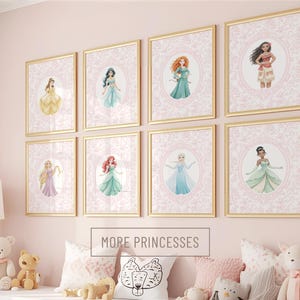 Peut inclure: Neuf impressions d'art de princesses encadrées avec des cadres dorés sont exposées sur un mur rose. Chaque impression présente une illustration de princesse dans un ovale rose, entourée d'une bordure décorative. Le texte "MORE PRINCESSES" est en dessous.