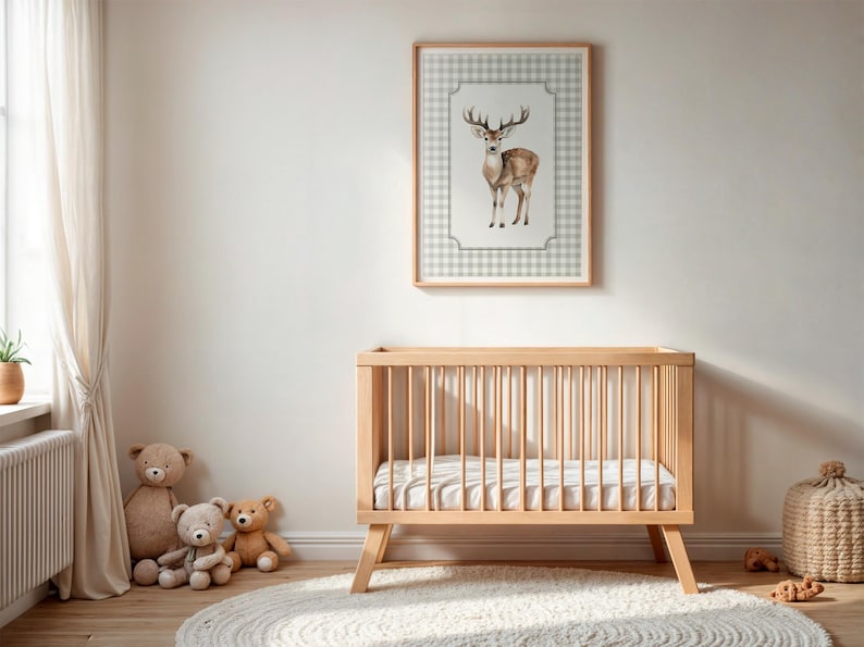 May include: A light wood baby crib with a mattress, a framed deer print, and teddy bears. The deer print features a watercolor illustration of a deer on a checkered background. The room has a neutral color palette.